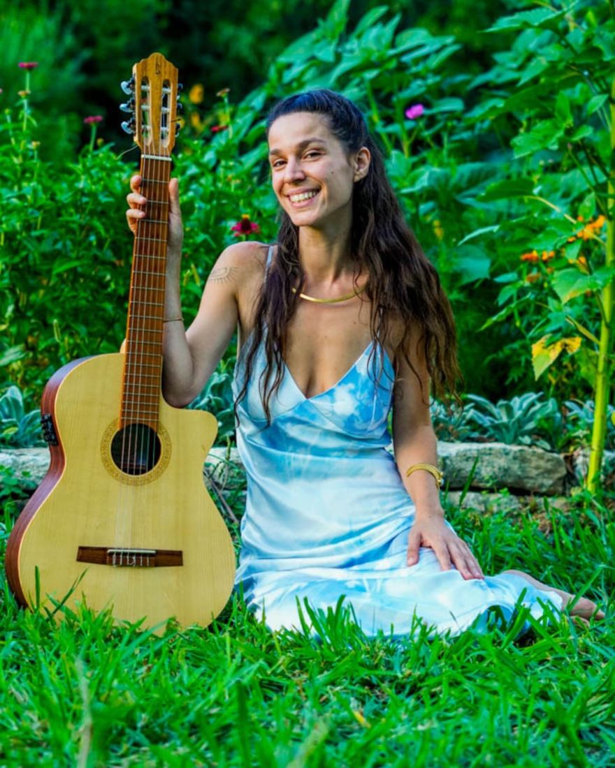 Benvinda sentada na relva com a sua guitarra, vestido azul